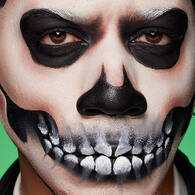 Look teschio di Halloween di NYX Professional Makeup con orbite nere, dettaglio del naso scheletrico e denti dipinti sulla bocca.