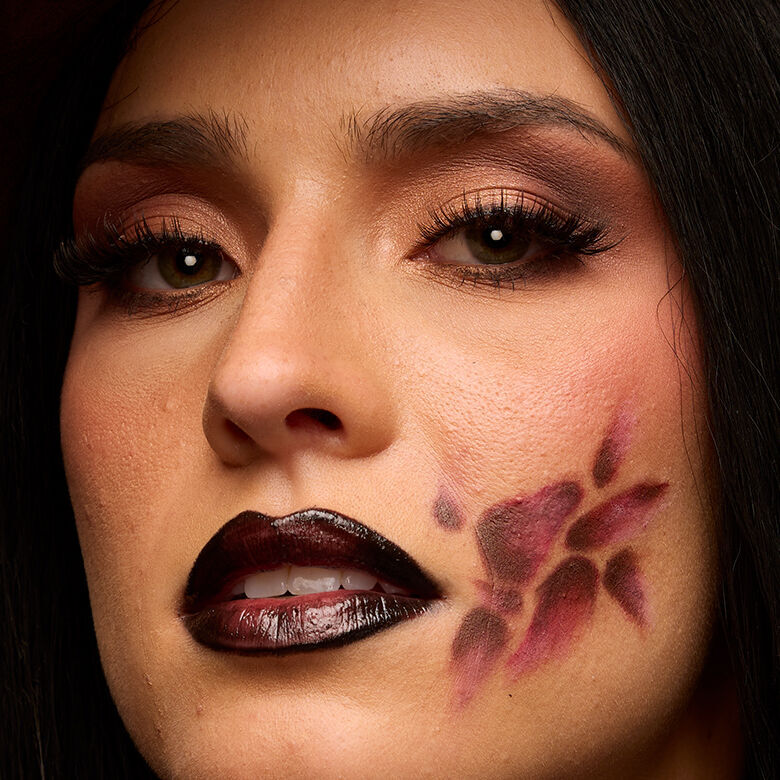 Look arancione e nero di Halloween di NYX Professional Makeup con un grande disegno grafico per gli occhi dipinto su tutto il viso e labbra nere lucide.