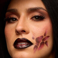 Look arancione e nero di Halloween di NYX Professional Makeup con un grande disegno grafico per gli occhi dipinto su tutto il viso e labbra nere lucide.