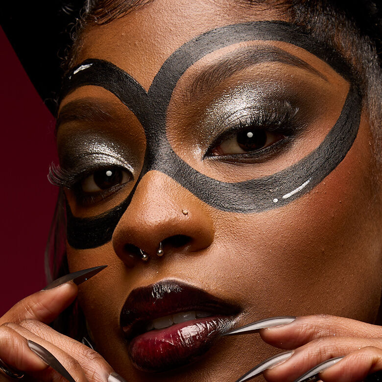  Look celestiale di Halloween di NYX Professional Makeup con pelle marrone lucida, puntini bianchi simili a stelle, ombretto metallizzato e un dettaglio grafico bianco sulla guancia