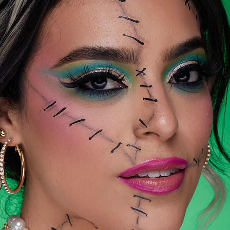 Look scheletro turchese di Halloween di NYX Professional Makeup con trucco occhi blu vivido, linee di contouring nere e denti scheletrici dipinti.