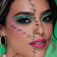 Look scheletro turchese di Halloween di NYX Professional Makeup con trucco occhi blu vivido, linee di contouring nere e denti scheletrici dipinti.