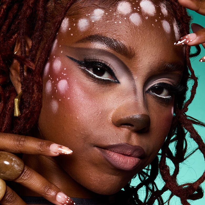 Look di Halloween dai toni caldi di NYX Professional Makeup con trucco pesca, segni rossi e viola sulle guance, sopracciglia definite e labbra nude.