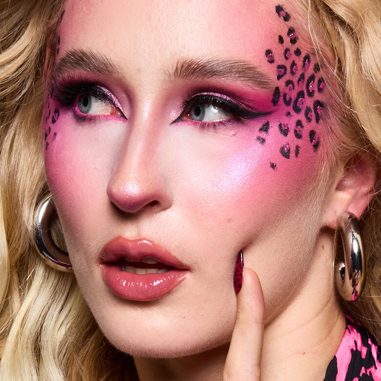 Look di Halloween ispirato al leopardo rosa di NYX Professional Makeup con ombretto rosa acceso, labbra rosa lucide e macchie di leopardo nere sulla guancia.