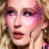 Look di Halloween ispirato al leopardo rosa di NYX Professional Makeup con ombretto rosa acceso, labbra rosa lucide e macchie di leopardo nere sulla guancia.