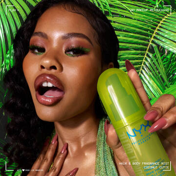 La modella tiene lo spray profumato capelli e corpo NYX Professional Makeup Coconut Cutie in un flacone verde neon su uno sfondo di foglie di palma tropicali