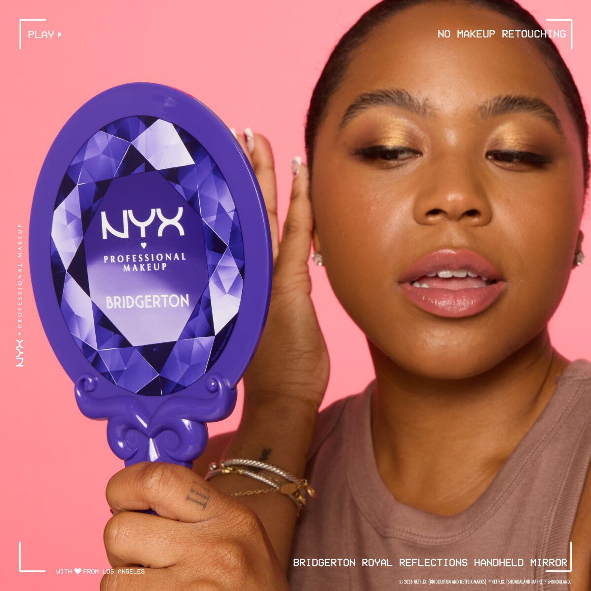 NYX Professional Makeup Bridgerton Royal Reflections Handheld Mirror tenuto in mano, che mostra il manico viola decorato e la confezione, escludendo il viso sfocato.