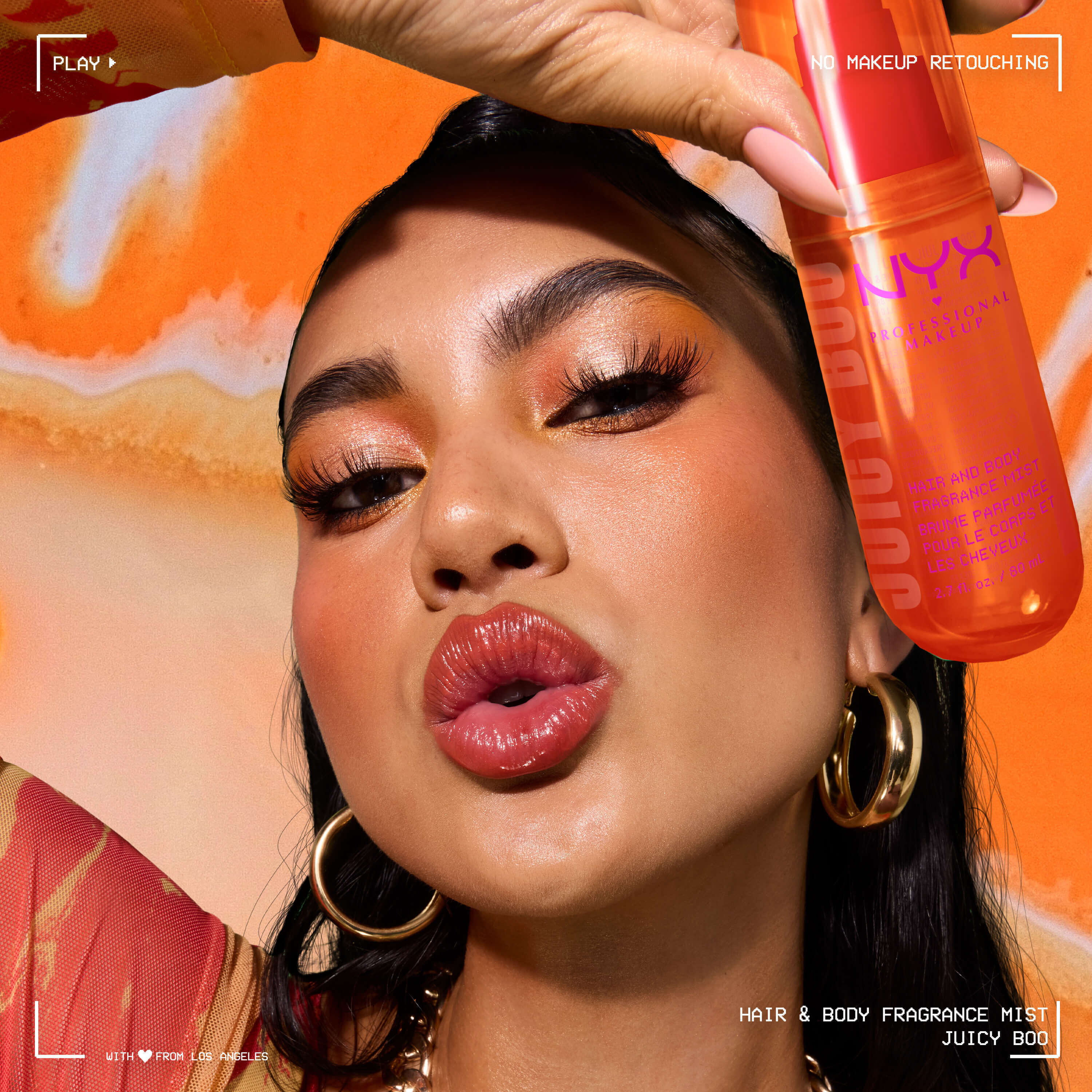 La modella tiene lo spray profumato capelli e corpo NYX Professional Makeup Juicy Boo in un flacone arancione acceso su sfondo arancione.