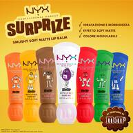 Sette tubetti di NYX Professional Makeup M&M'S Smushy Soft Matte Lip Balm in colori assortiti su sfondo giallo, con testo che sottolinea la sensazione di un balsamo, texture delle labbra levigata (effetto blurred), colore velato modulabile e profumo di M&M'S.